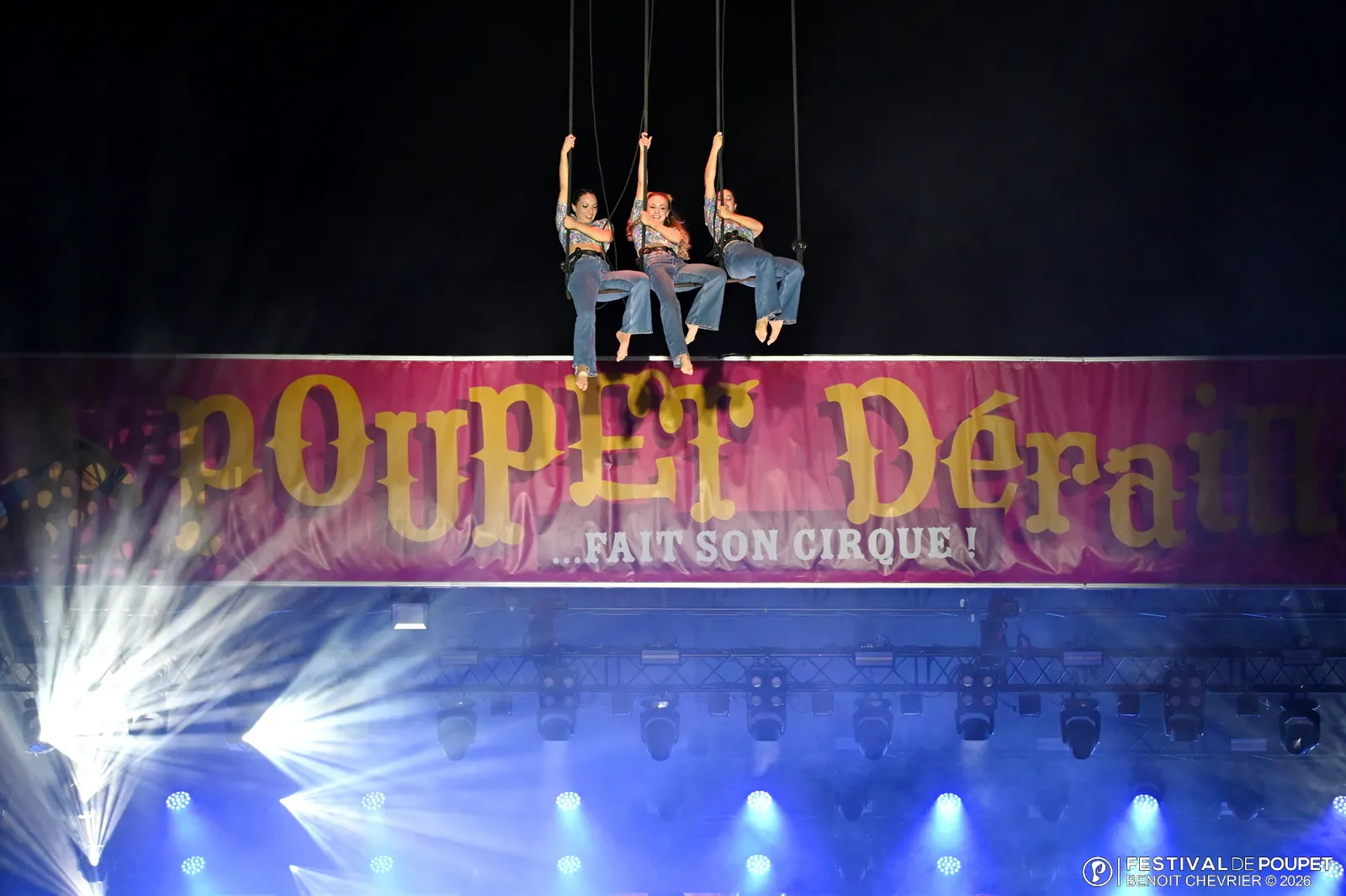 Voltigeurs suspendus devant la banderole géante « Poupet Déraille fait son cirque », faisceaux de lumière